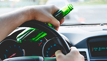A person driving a car while holding a beer bottle in their right hand